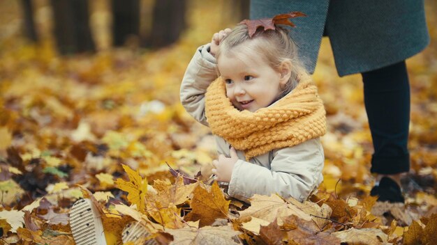 Маленькая дочь играет с желтыми листьями в осеннем парке, девочка счастлива и смеется