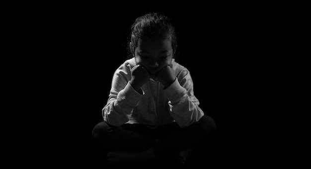 Little daughter sitting while holding her legs in sad emotion.\
depression and sad concept against black background