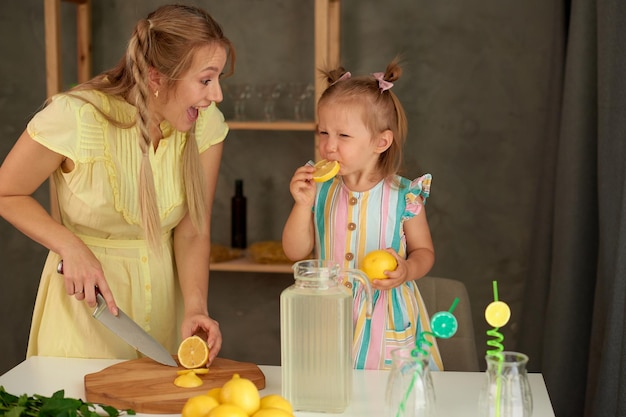 Little daughter taste slice of lemon with mother in kitchen girls reaction of very sour lemon