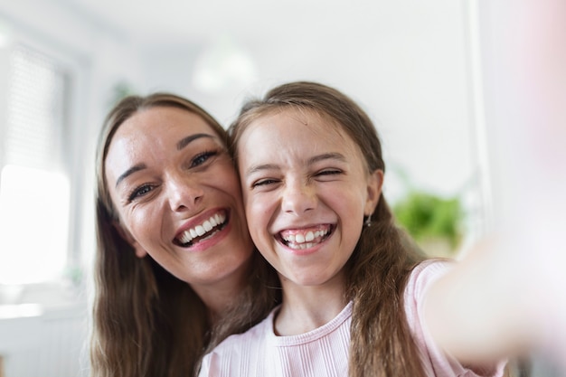 Little daughter young mother faces webcam close up view. Adorable kid girl use smartphone have fun with older sister making selfie photography, vloggers record new vlog, enjoy funny activity concept