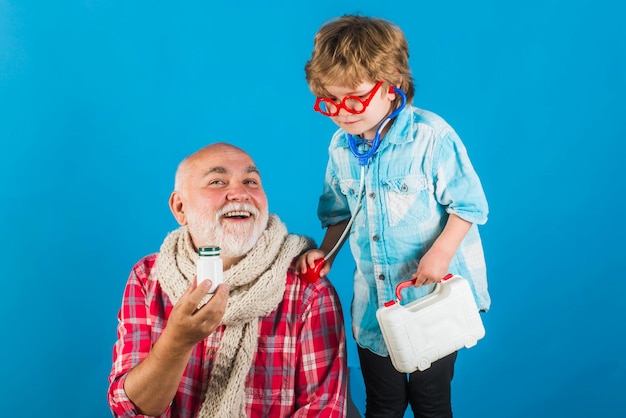 Little doctor giving grandfather medicament Man in knitted colorful scarf with medicine Smiling grandfather and his grandson playing with a stethoscope