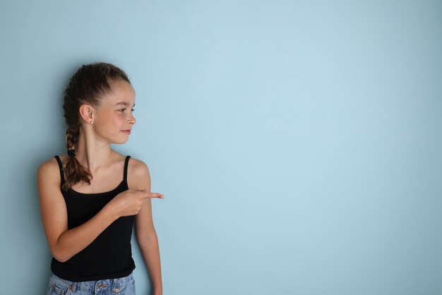 검정 티셔츠를 입은 감정적인 10대 소녀 11세 12세는 고립된 파란색 배경의 Children39s 스튜디오 초상화에 비문을 위한 장소를 복사하기 위해 텍스트를 배치합니다.