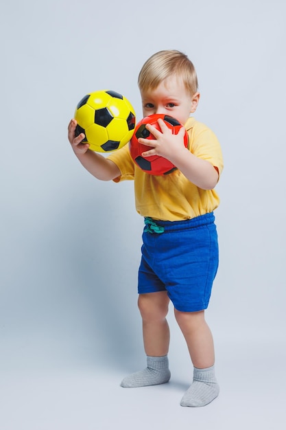 Little european boy fan or player in yellow and blue uniform with a soccer ball supports the soccer team on a white background Football sport game lifestyle concept Isolated on white background