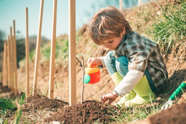 シャベルとじょうろを持った小さな農夫は庭の小さな助っ人花を植える子供農夫は野菜の庭に植える