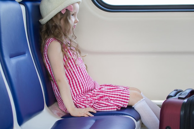 Little fashionable girl sitting on armchair near the window in the train