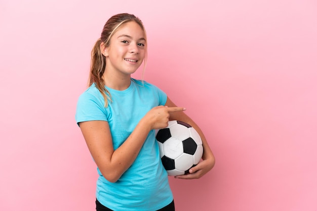 Little football player girl isolated on pink background pointing finger to the side