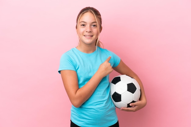 Little football player girl isolated on pink background pointing to the side to present a product