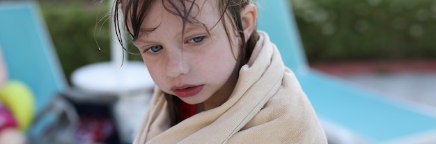 Little frozen girl sits on beach in towel