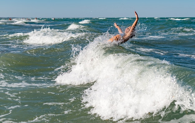 Фото Маленькая забавная активная счастливая девушка плещется в шумных морских волнах в солнечный теплый летний день. концепция отдыха на море с детьми.