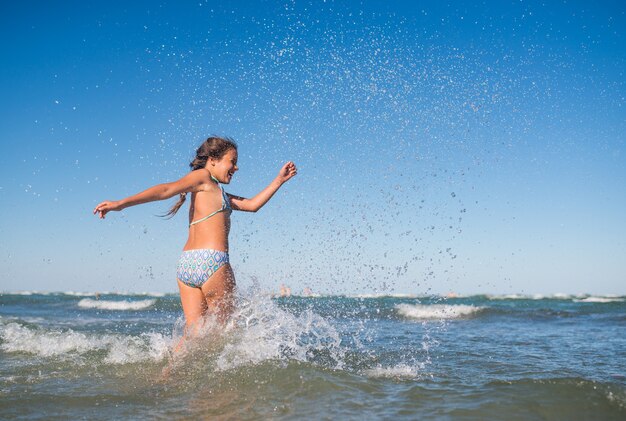 日当たりの良い暖かい夏の日に騒々しい海の波に飛び散る小さな面白いアクティブな幸せな女の子