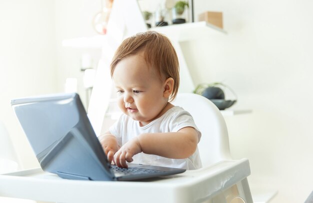 Little funny baby girl typing on a netbook while sitting at the childrens table at home