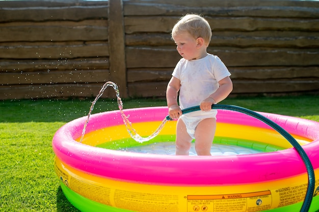 Little funny boy collecting water in the children's swimming pool