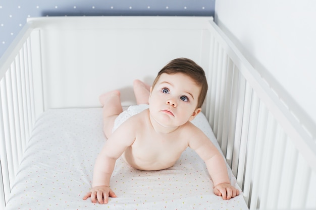 Little funny boy lying in baby bed with shocked face expression