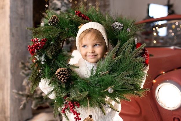 Little funny boy playing with Christmas wreath.