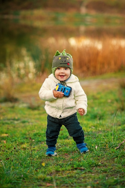 A little funny boy with two teeth in warm clothes playing near the lake on the sunset.
