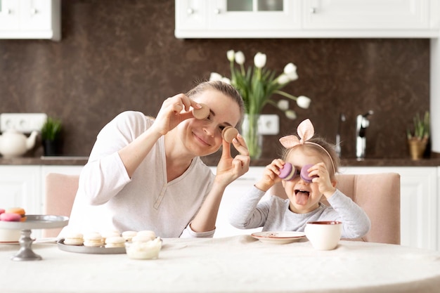 Piccola bambina divertente e sua madre bevono tè o caffè con dolci amaretti e giocano