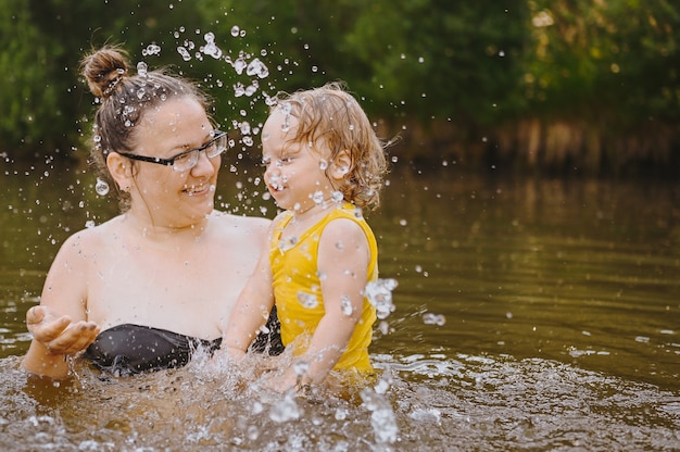 Photo little funny cute blonde girl child toddler in yellow bodysuit laughing learns swim outside at