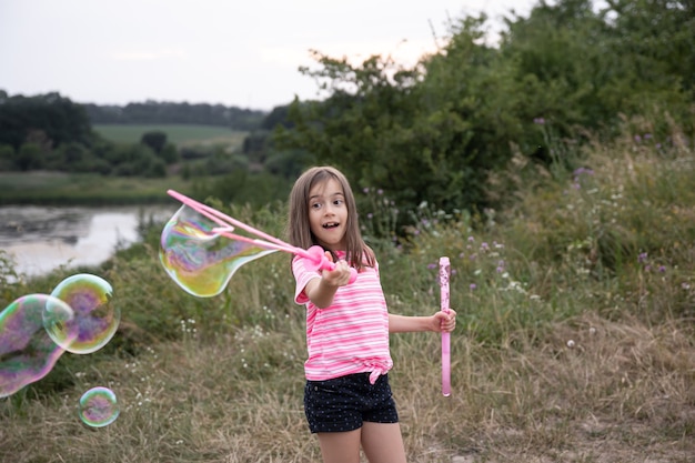 A little funny girl blows soap bubbles in the summer in a field, outdoor summer activities.