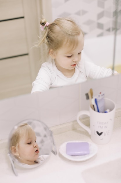 little funny girl brushing teeth and washing hands in the bathroom reflection in the mirror