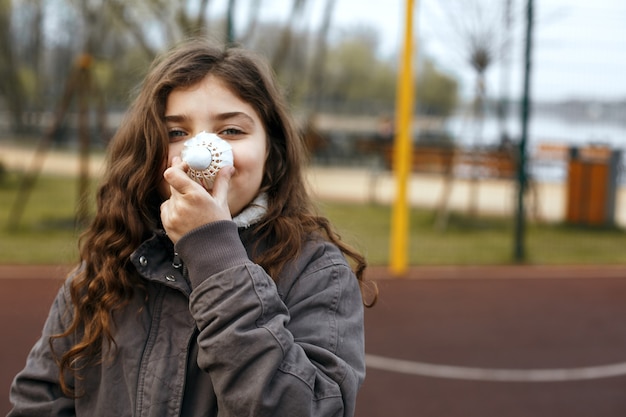 Little funny girl holding shuttlecock for badminton near her nose. Empty space