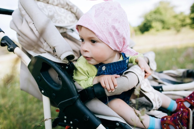 Little funny girl sits in a stroller in the park