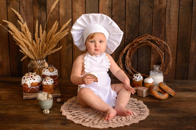 A little funny girl in a white cook suit on a dark wooden background Preparation for Easter