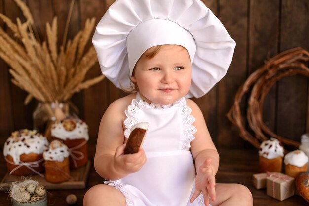 A little funny girl in a white cook suit on a dark wooden background Preparation for Easter