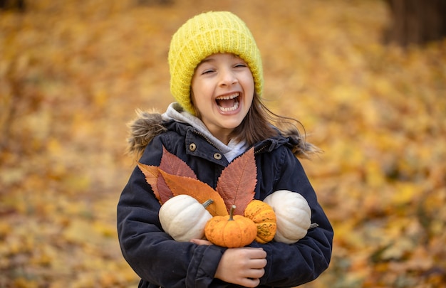 Bambina divertente con le zucche nella foresta autunnale su uno sfondo sfocato.