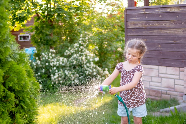 Little gardener girl, she is watering flowers on the lawn near cottage