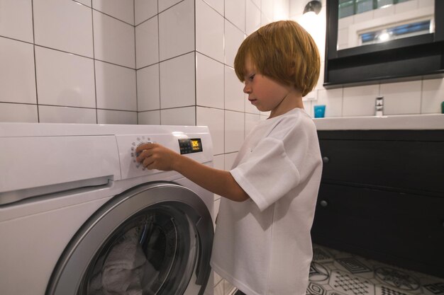Маленький рыжий мальчик включает стиральную машину