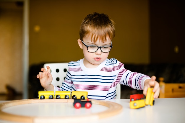 Little ginger child boy in the glasses with syndrome dawn playing with wooden railways