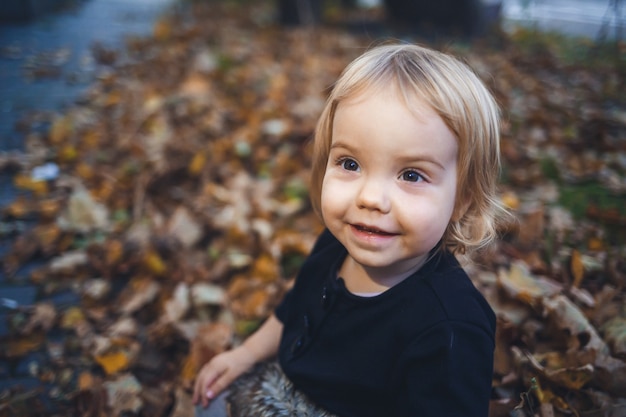 A little girl of 1.5 years is standing and smiling. The child throws leaves. Cheerful girl in the autumn forest