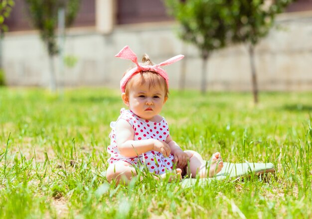 Little girl 11 months old is sitting in the park on the grass. baby girl in a jacket in peas sits on the grass and plays with soap bubbles.