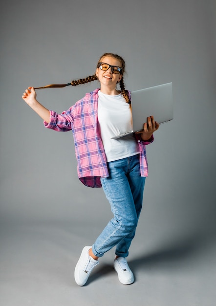 Little girl 12-13 years old, holding a laptop isolated on a gray background. Copy space for copy.