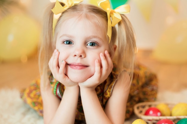 Фото Маленькая девочка 3-х лет лежала на полу с ярко-желтой одеждой с пасхальными яйцами
