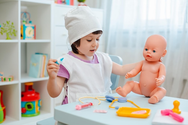 Little girl 3 years old preschooler playing doctor with doll The child makes an injection toy