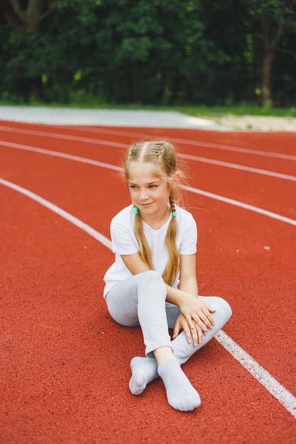 Una bambina di 78 anni con una maglietta bianca corre all'aperto nello stadio la ragazza sta facendo sport in una giornata di sole