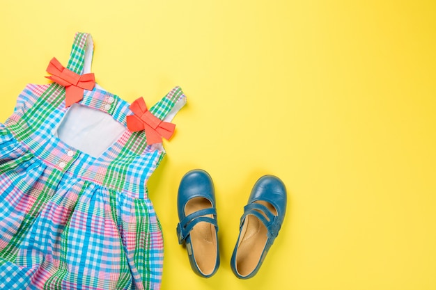 Little girl accessories. Colorful dress and shoes on yellow surface.