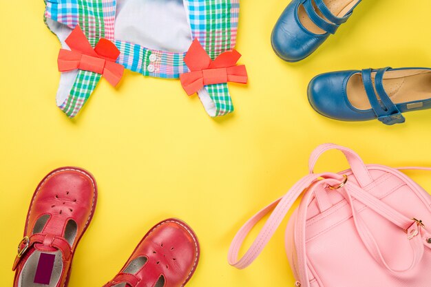 Little girl accessories. Pink bag with colorful dress and shoes on yellow surface. 