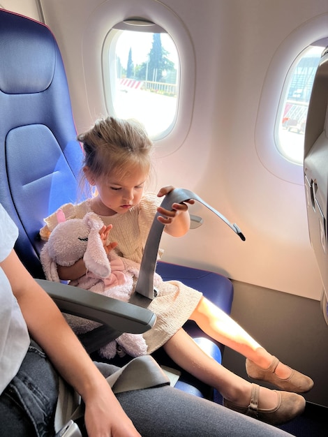 Маленькая девочка в кресле самолета осматривает ремень безопасности