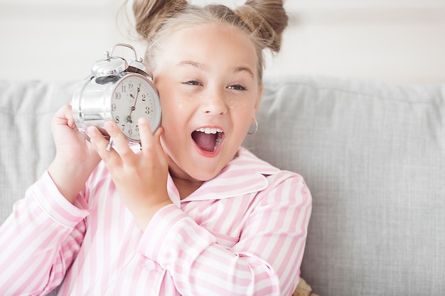 Little girl and alarm clock. Funny child with clock in the morning.