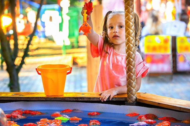 a little girl in the amusement park plays children's fishing, catches toy fish