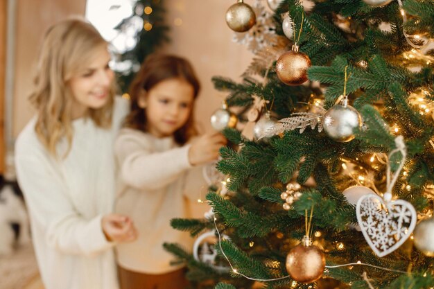 Фото Маленькая девочка и ее мама веселятся рядом с рождественской елкой