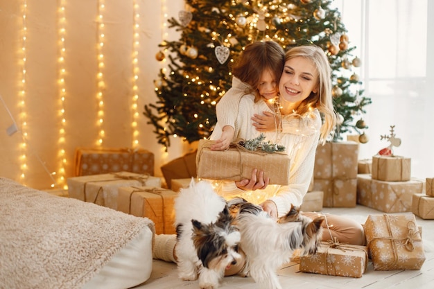 Фото Маленькая девочка и ее мама сидят возле рождественской елки с йоркширскими терьерами