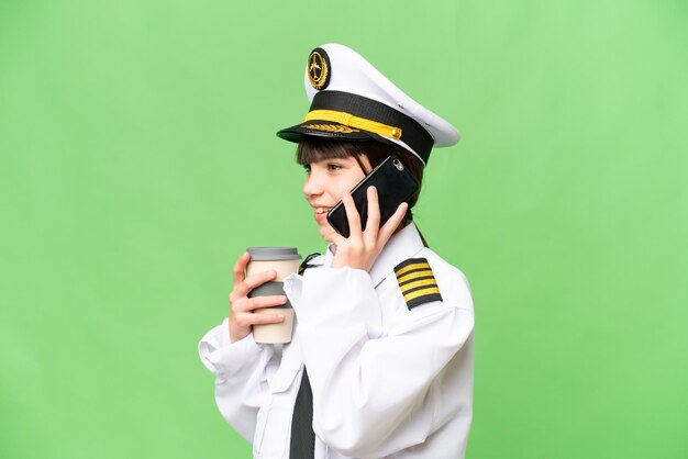 Little girl as a Airplane pilot over isolated chroma key background holding coffee to take away and a mobile