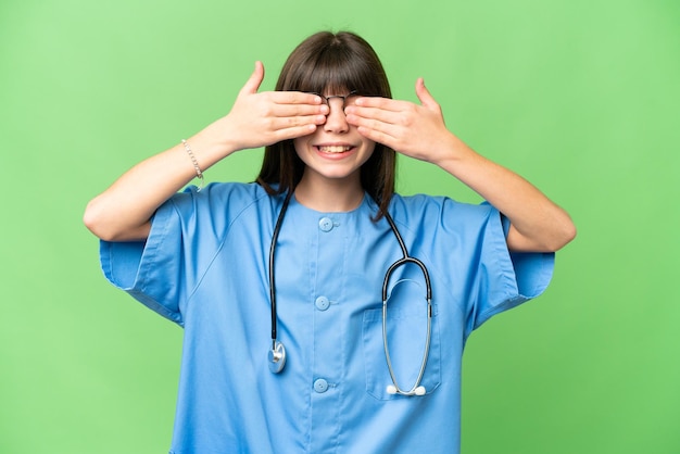 Little girl as a surgeon doctor over isolated chroma key background covering eyes by hands