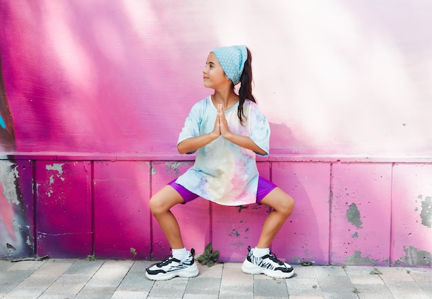 A little girl athlete does gymnastics on the street against a\
pink wall generation z healthy lifestyle