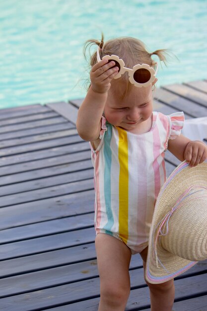 美しいスイムスーツとサングラスを着たプールの背景にある小さな女の子