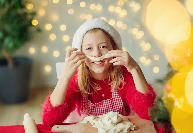 小さな女の子はクリスマスのクッキーを焼き、変な顔をします