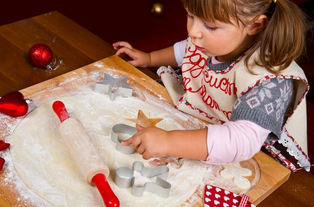 Little girl baking Christmas cookies cutting pastry with a cooki